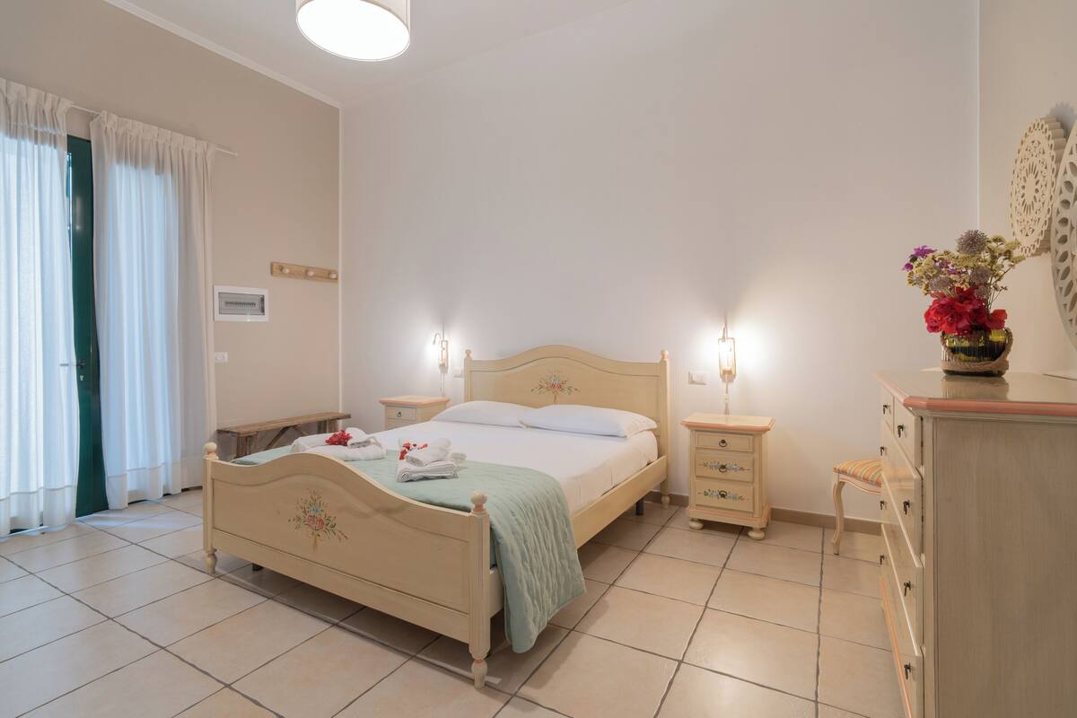 Une chambre à coucher avec un lit, des tables de chevet, une commode et une fenêtre avec des rideaux.