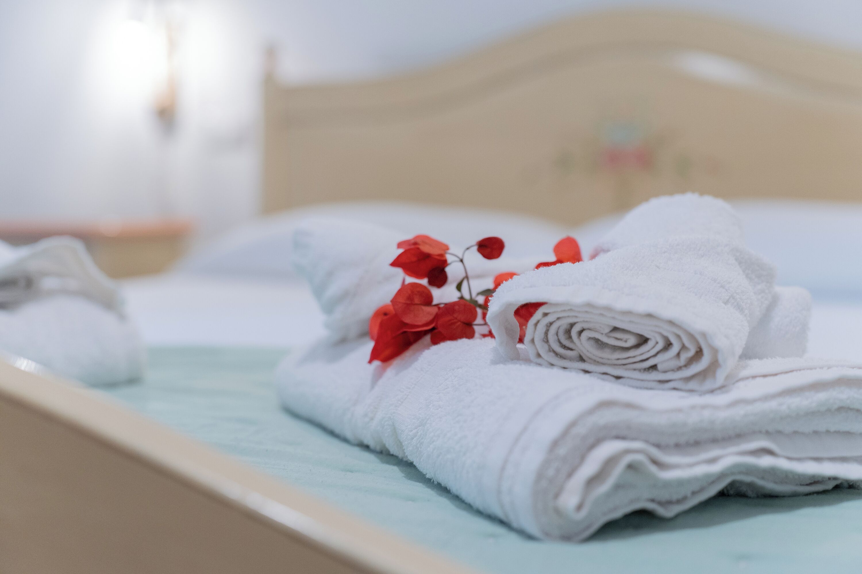 A neatly made bed with white towels and red flowers.