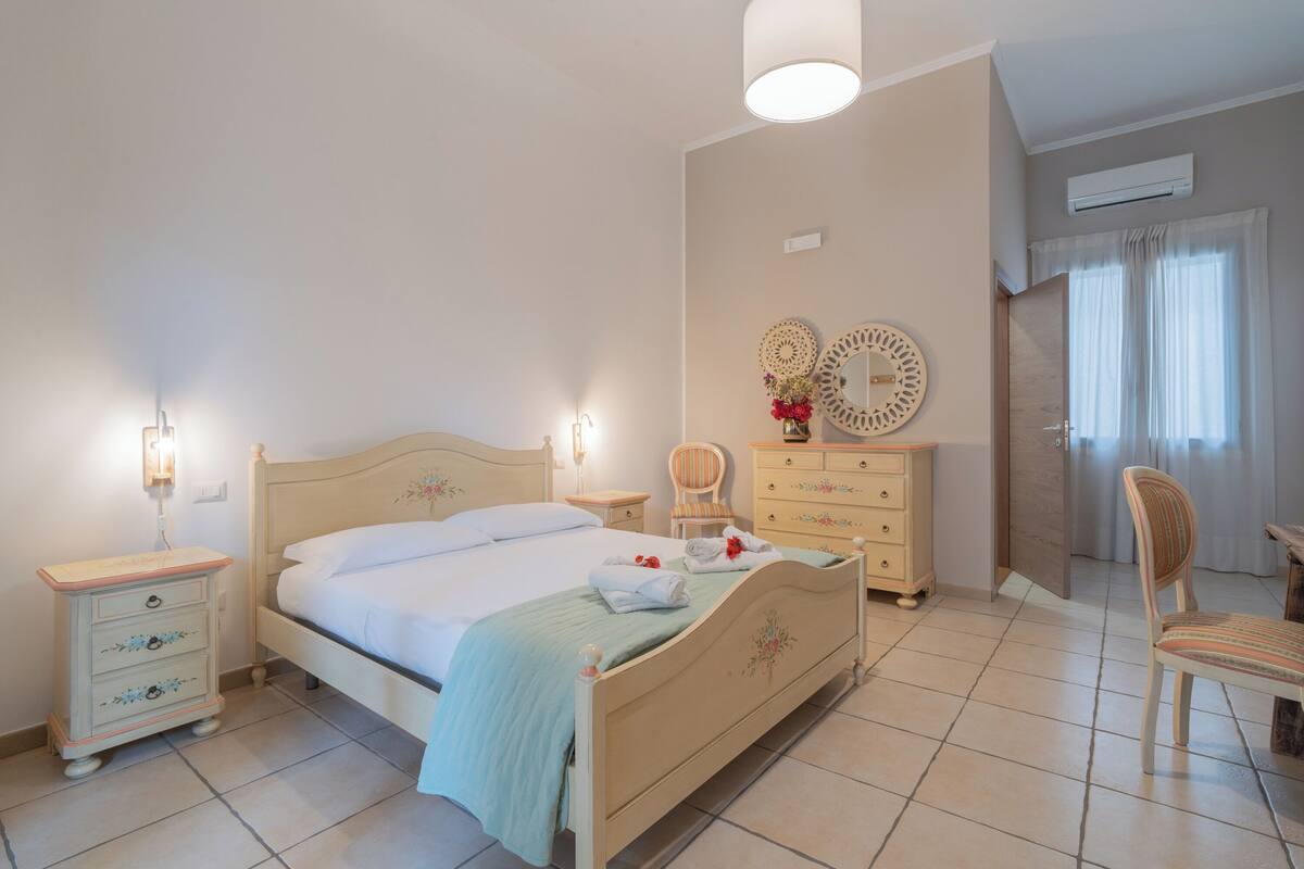 Une chambre à coucher comprenant un lit, des tables de chevet, une commode, une chaise et un miroir.