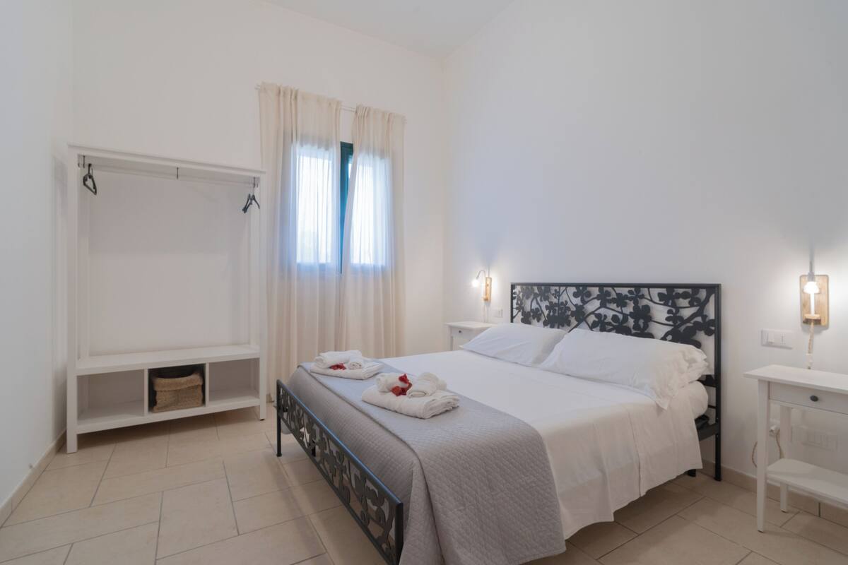 Une chambre bien rangée, avec un lit, des tables de chevet, une armoire et une fenêtre avec des rideaux.