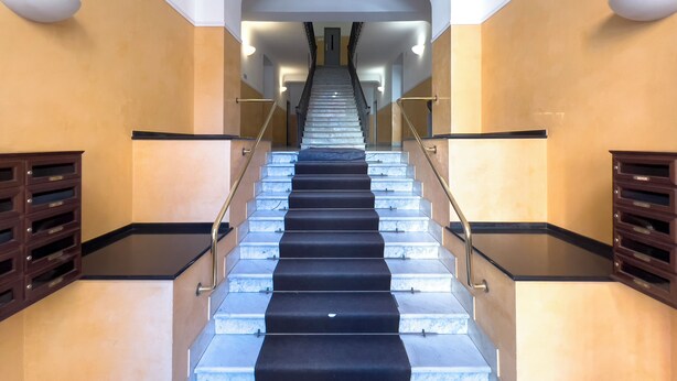 A grand staircase with marble steps and black carpet, flanked by wooden cabinets and glass railings. - Graceful Home Genova City Center (Genoa)