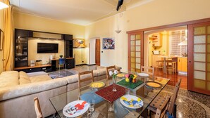 A modern living room with a sofa, TV, and dining area with a glass table. - Graceful Home Genova City Center (Genoa)