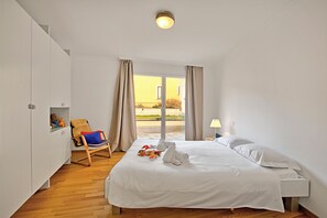 A hotel room with a large bed, a chair, a nightstand, and a view of the outside.
