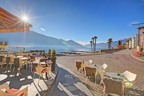 An outdoor café with tables and chairs, a view of the sea, and mountains in the background.