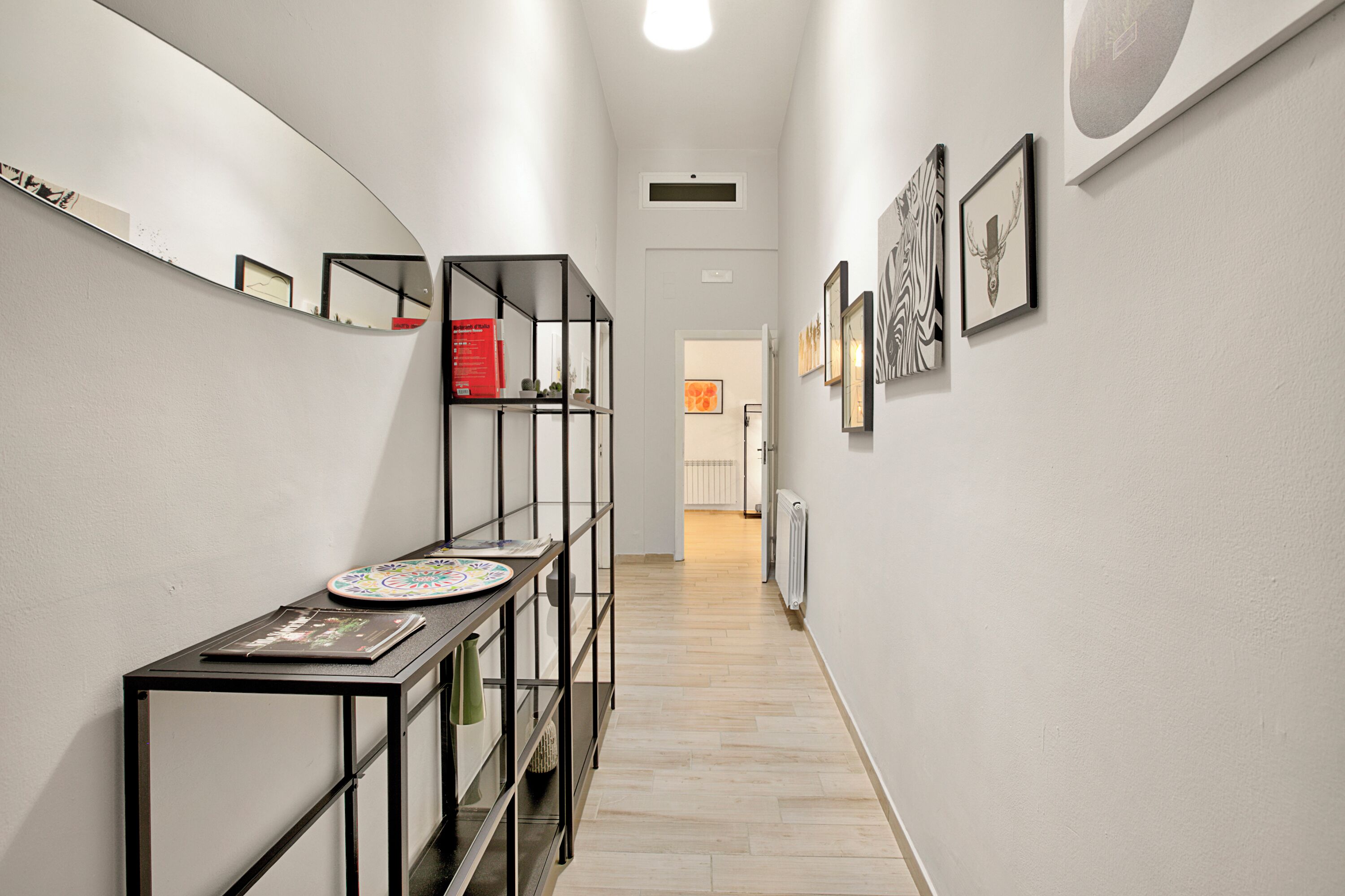 A hallway with a black metal console table, a mirror, and framed artwork on the walls.