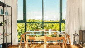 A dining area with a glass table and chairs, a bookshelf, and a view of greenery through large windows. -  Caesarea Sea Elegant Stay by Sea N' Rent (Hof HaCarmel)