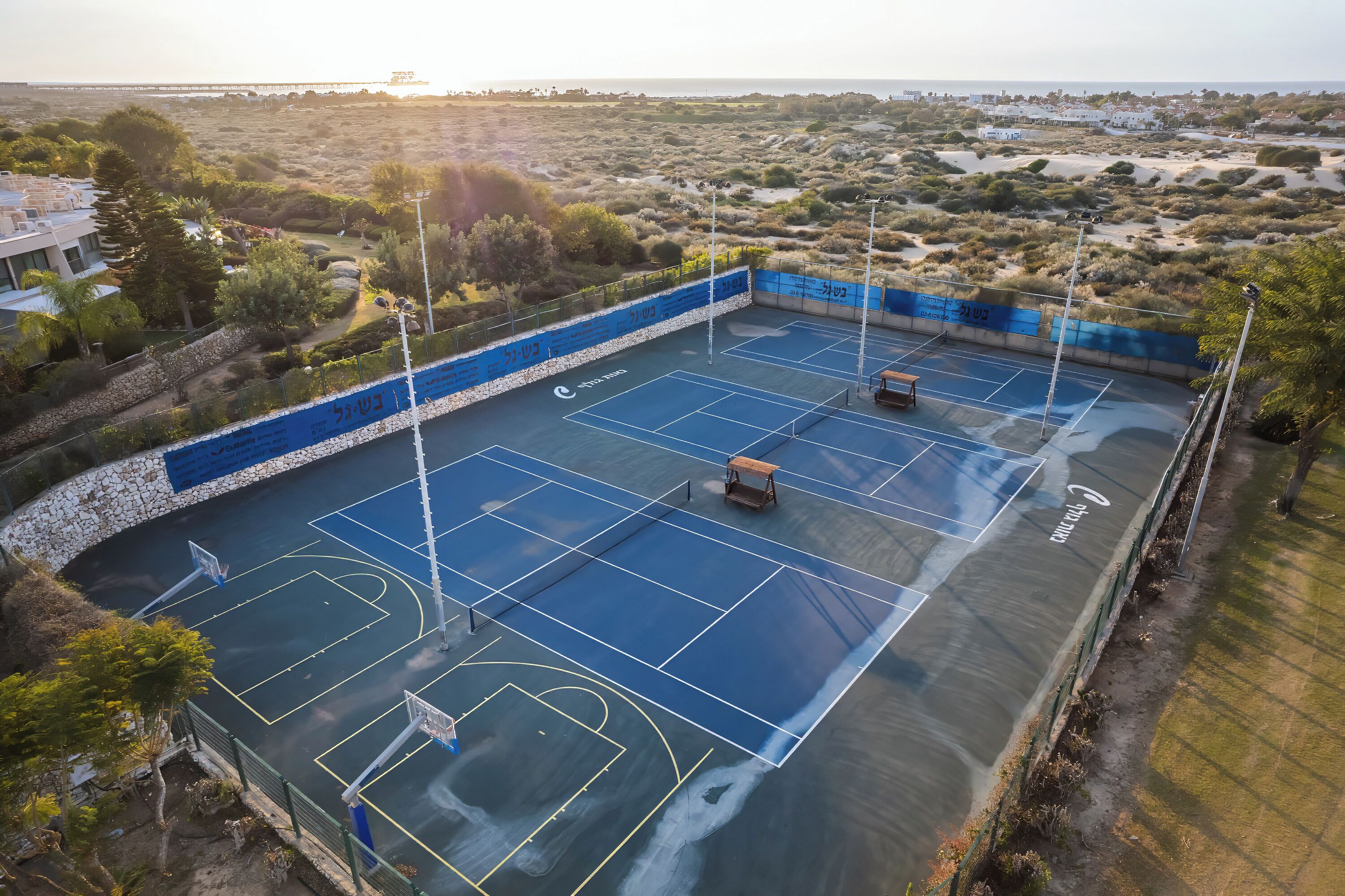 Una cancha de tenis al aire libre con un muro de piedra y una valla azul.