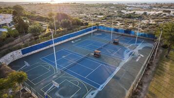 Una cancha de tenis al aire libre con un muro de piedra y una valla azul.