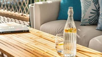 Una botella de vidrio transparente con una rodaja de limón sobre una mesa de madera, un vaso de agua y un libro titulado