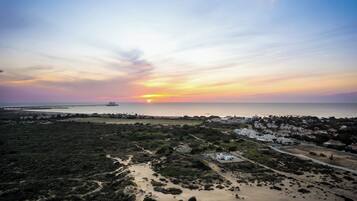 An aerial view of a coastal area with a sunset, a bridge, and a residential area with white buildings.