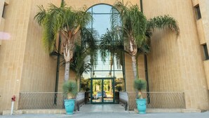 A building entrance with a glass door, flanked by palm trees and potted plants. -  Caesarea Sea Elegant Stay by Sea N' Rent (Hof HaCarmel)