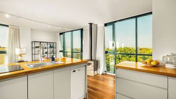 A modern kitchen with a wooden countertop, white cabinets, a dishwasher, and a large window offering a view of greenery and buildings.
