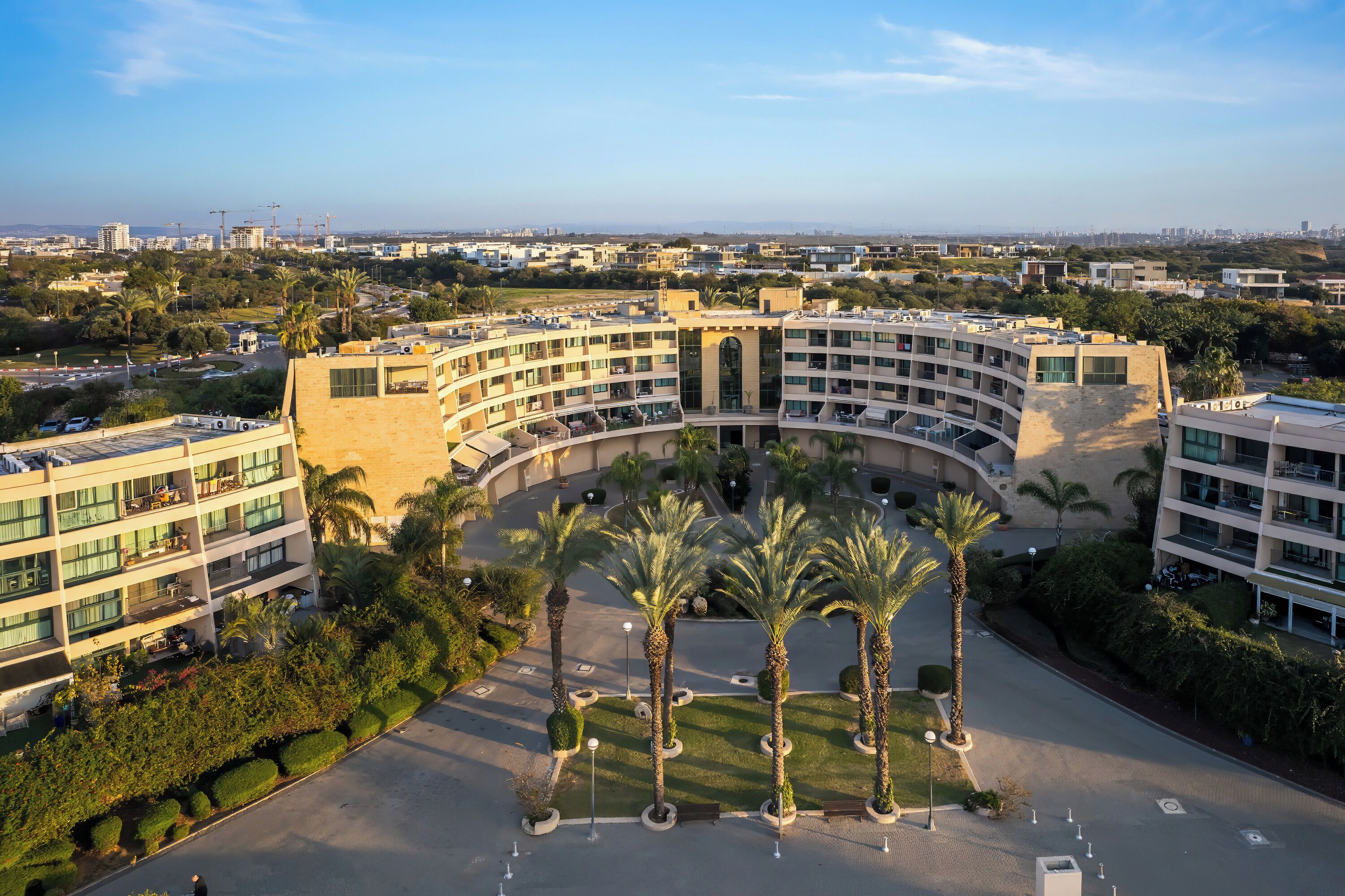A modern hotel with a curved facade, multiple balconies, and a central courtyard with palm trees.