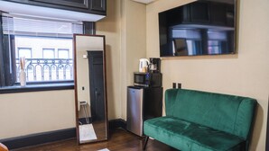 Un espacio habitable compacto con un sofá verde, una pequeña kitchenette con microondas y un espejo grande que refleja la habitación.