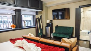 Habitación de hotel con cama, un sillón verde, escritorio con cafetera y vistas al balcón exterior.