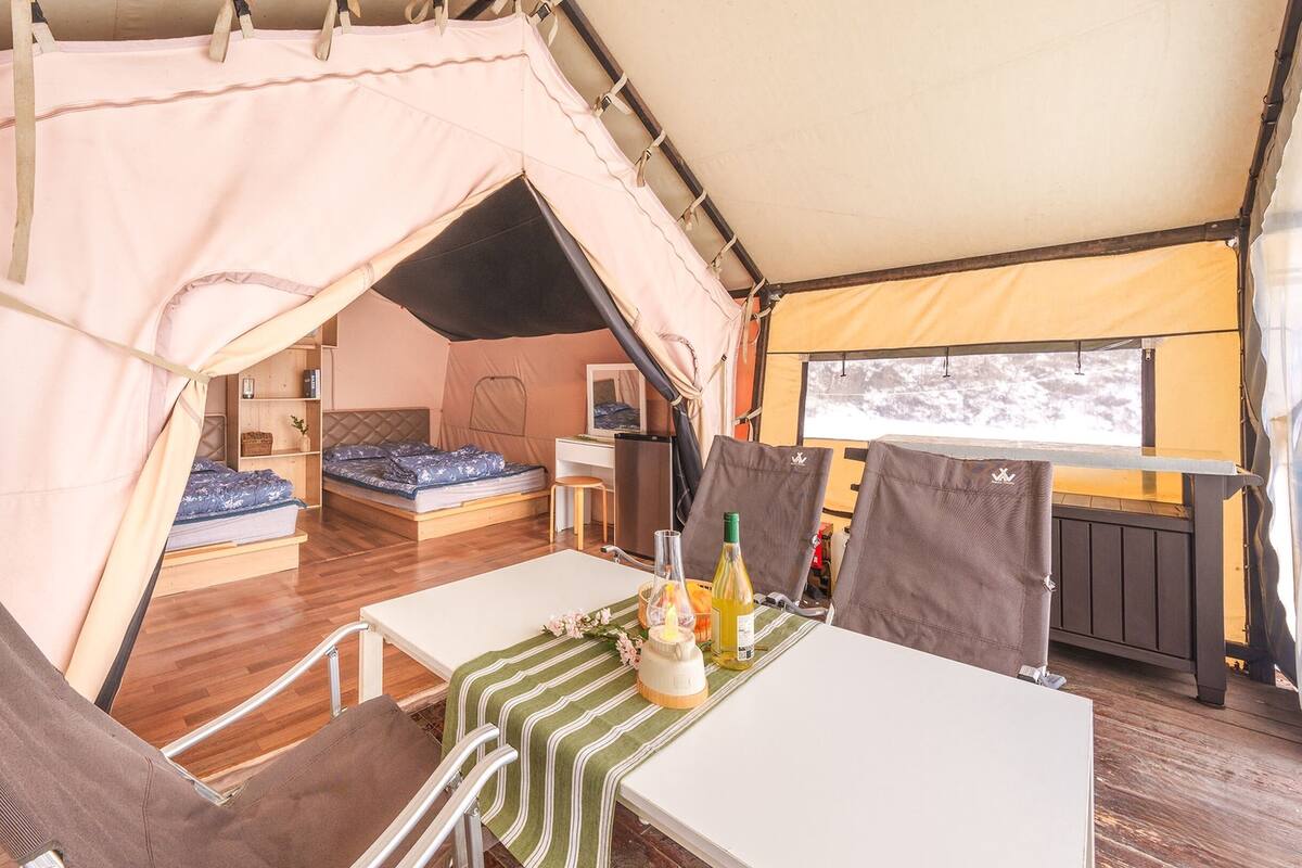 Alojamiento con carpa que incluye dos camas, una mesa de comedor y un refrigerador.