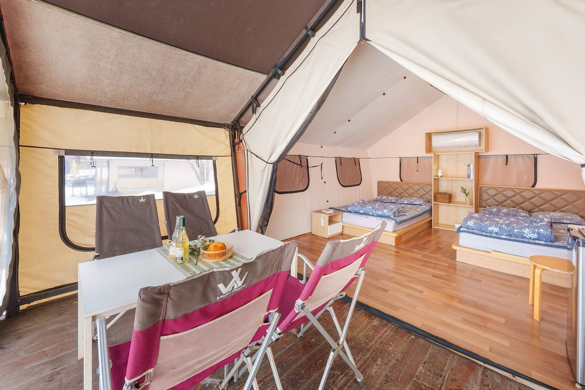 Alojamiento con carpa, zona de comedor, dos camas y una mesita.