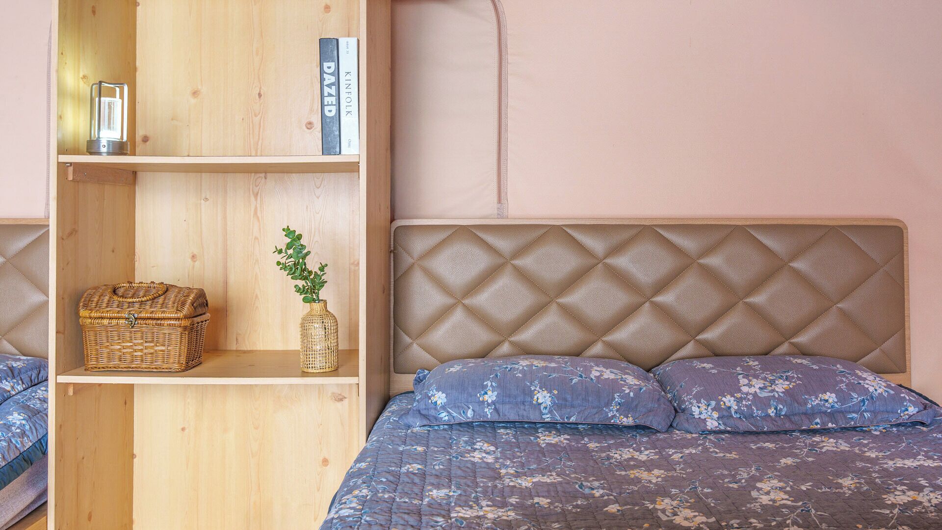 Un dormitorio con cabecera de madera, una estantería, una cesta de mimbre y un florero con una planta.
