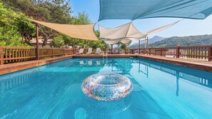 Une piscine aux eaux cristallines, agrémentée d’un flotteur circulaire, entourée d’une terrasse en bois et ombragée par une pergola.