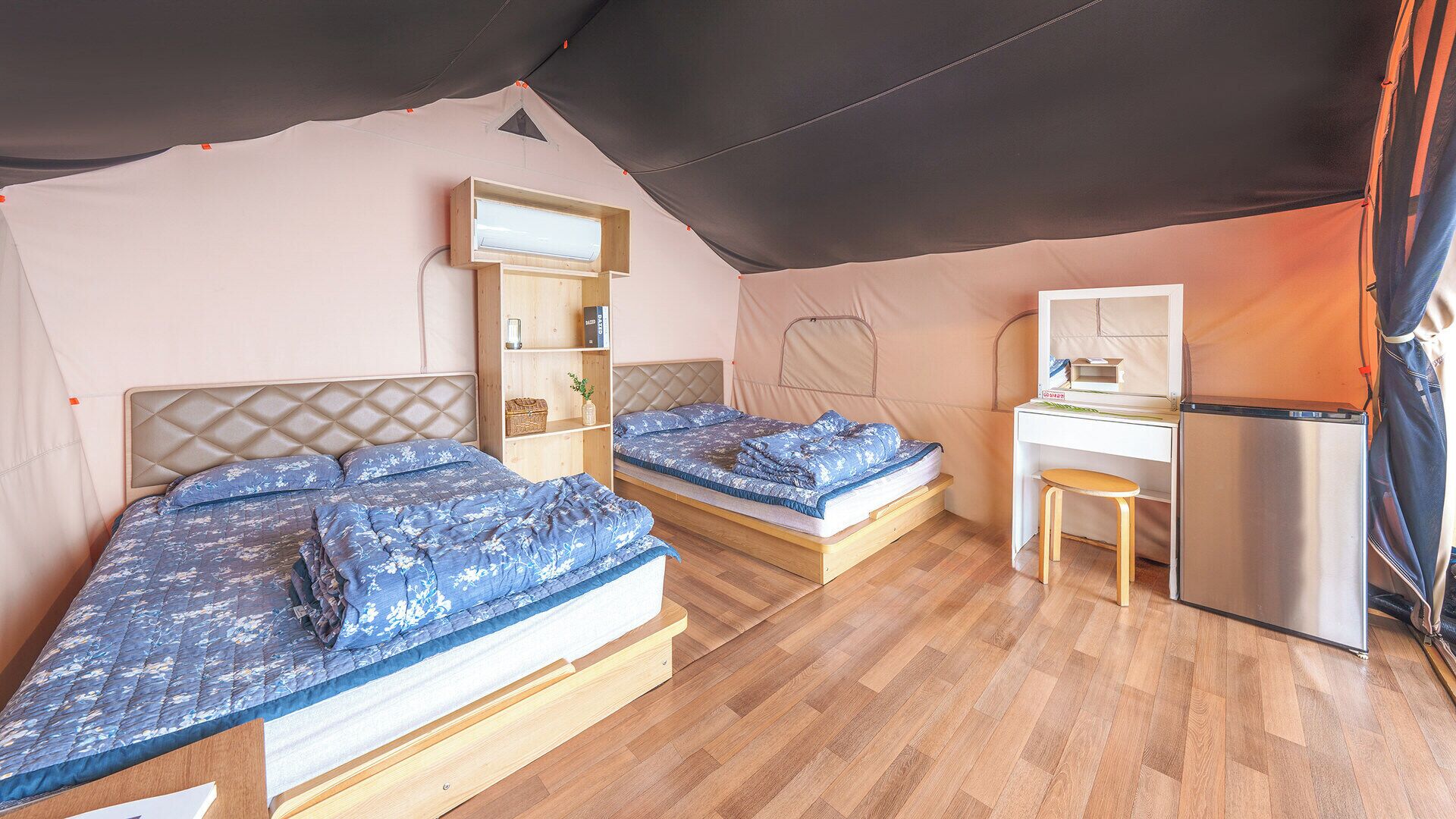 A tented accommodation with two beds, a desk, and a refrigerator.