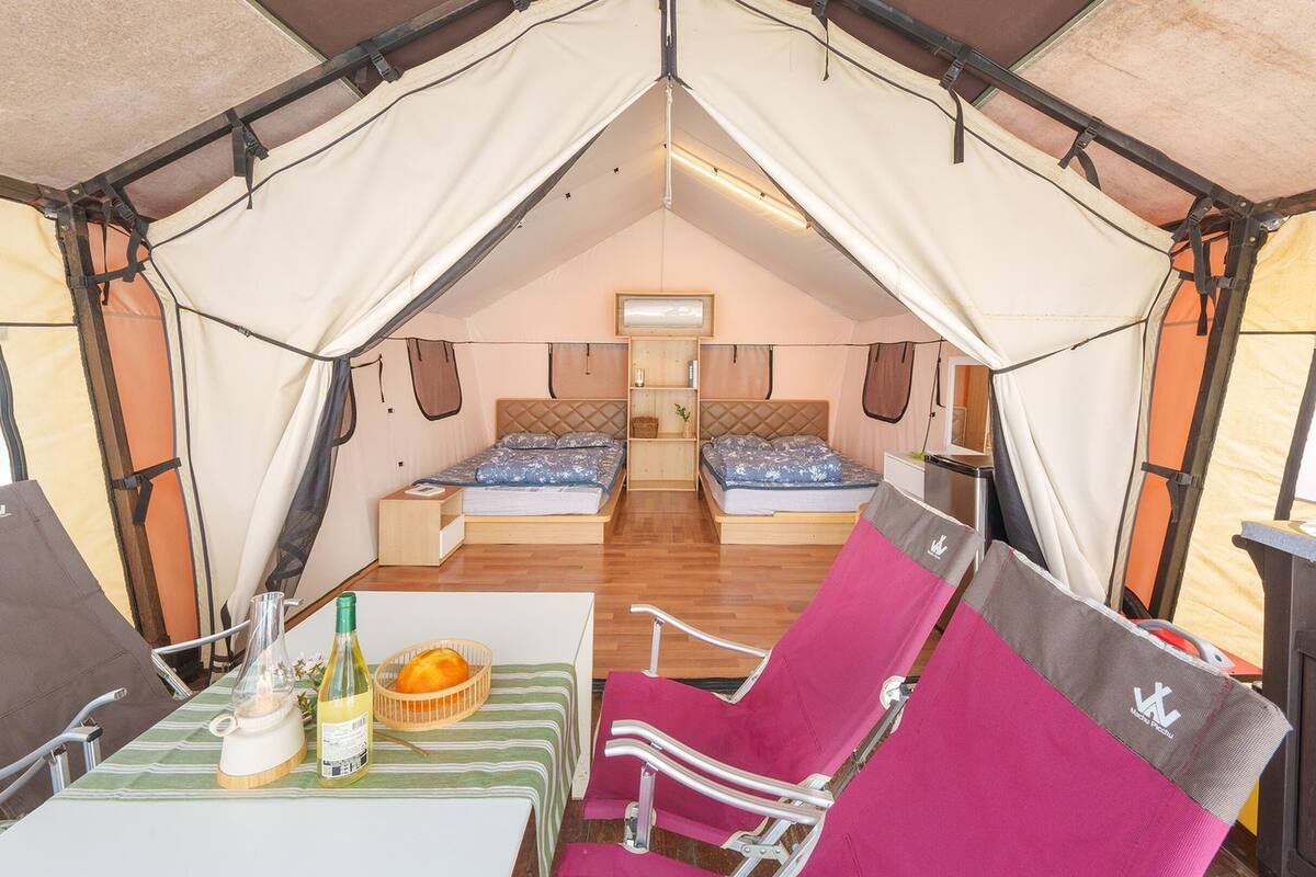 Un alojamiento en carpa con dos camas, una mesa con una botella y una cesta, y una silla con cojín.