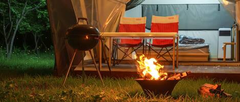 A tent with a grill and a fire pit in front.
