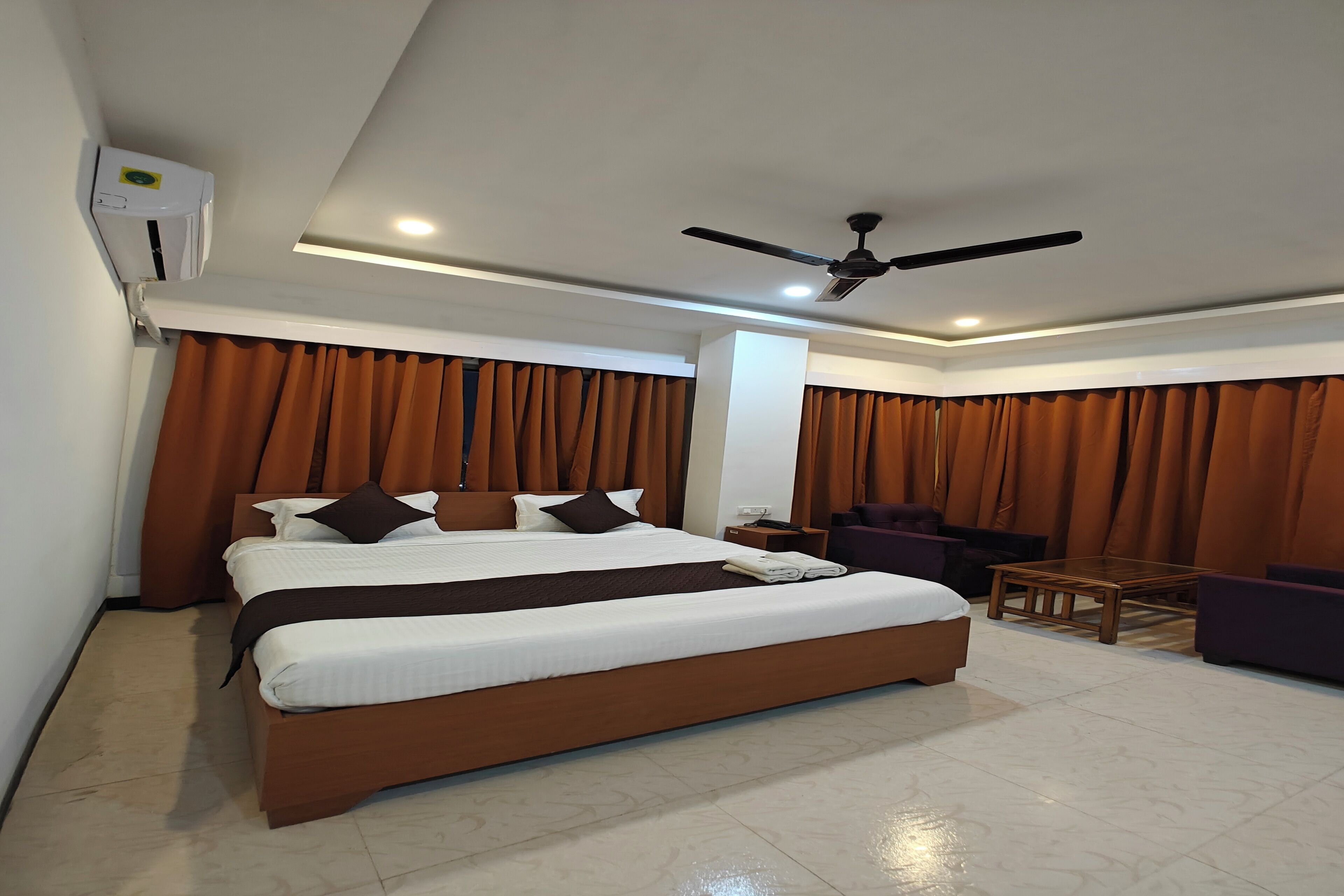 A hotel room with a large bed, a ceiling fan, and brown curtains.