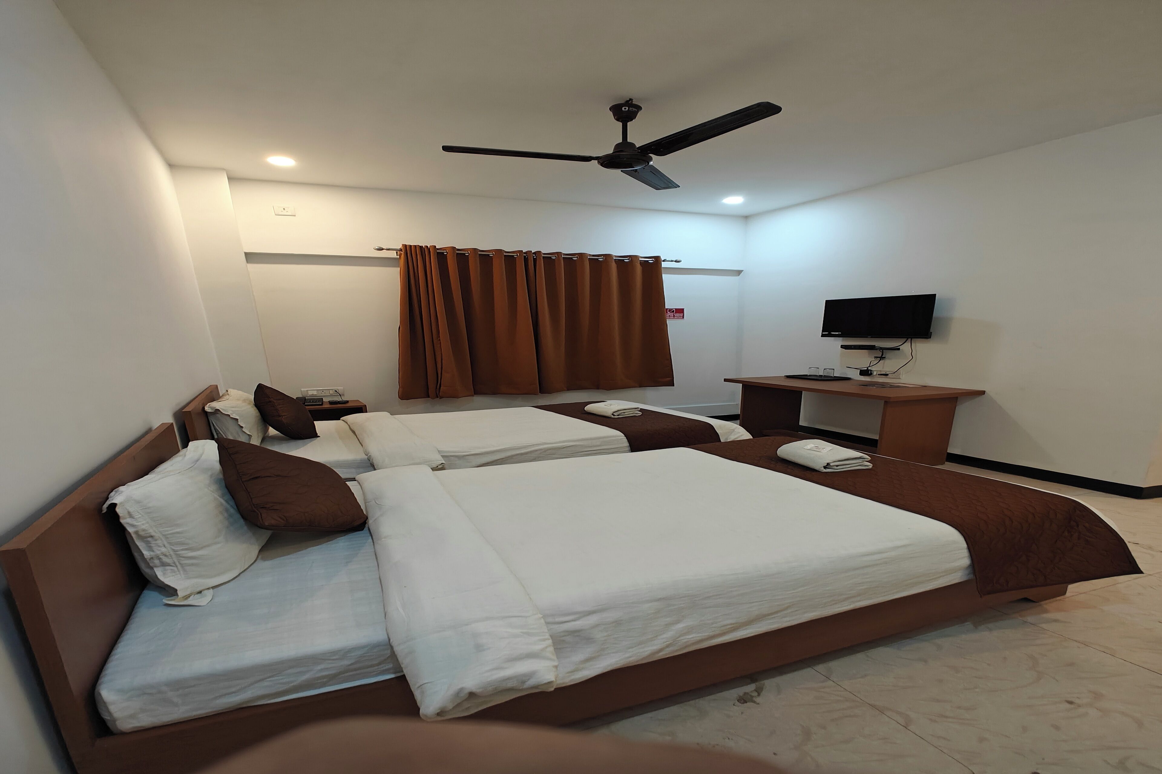 A hotel room with two beds, a ceiling fan, a TV, and a small desk.