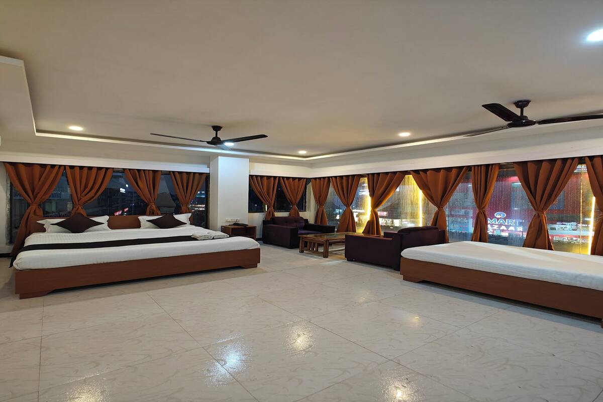 A hotel room with two beds, a sofa, a coffee table, and a view of the city at night.