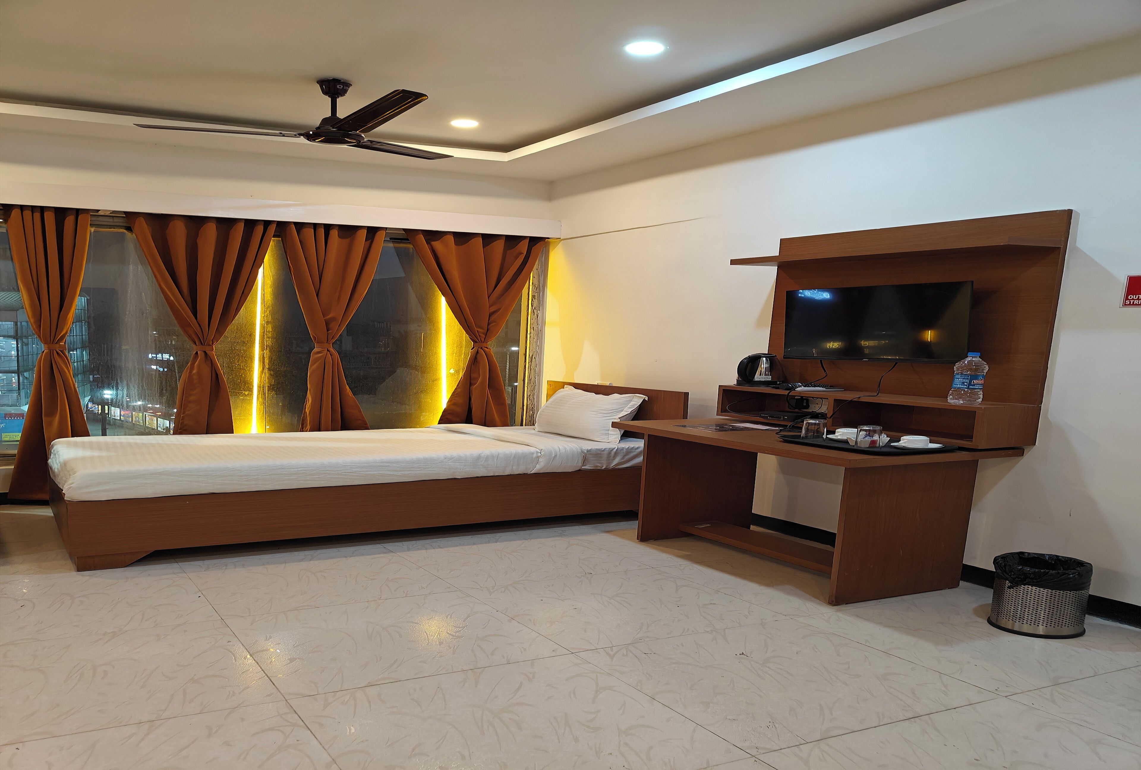 A modern hotel room with a large bed, a desk, a flat-screen TV, and a ceiling fan.
