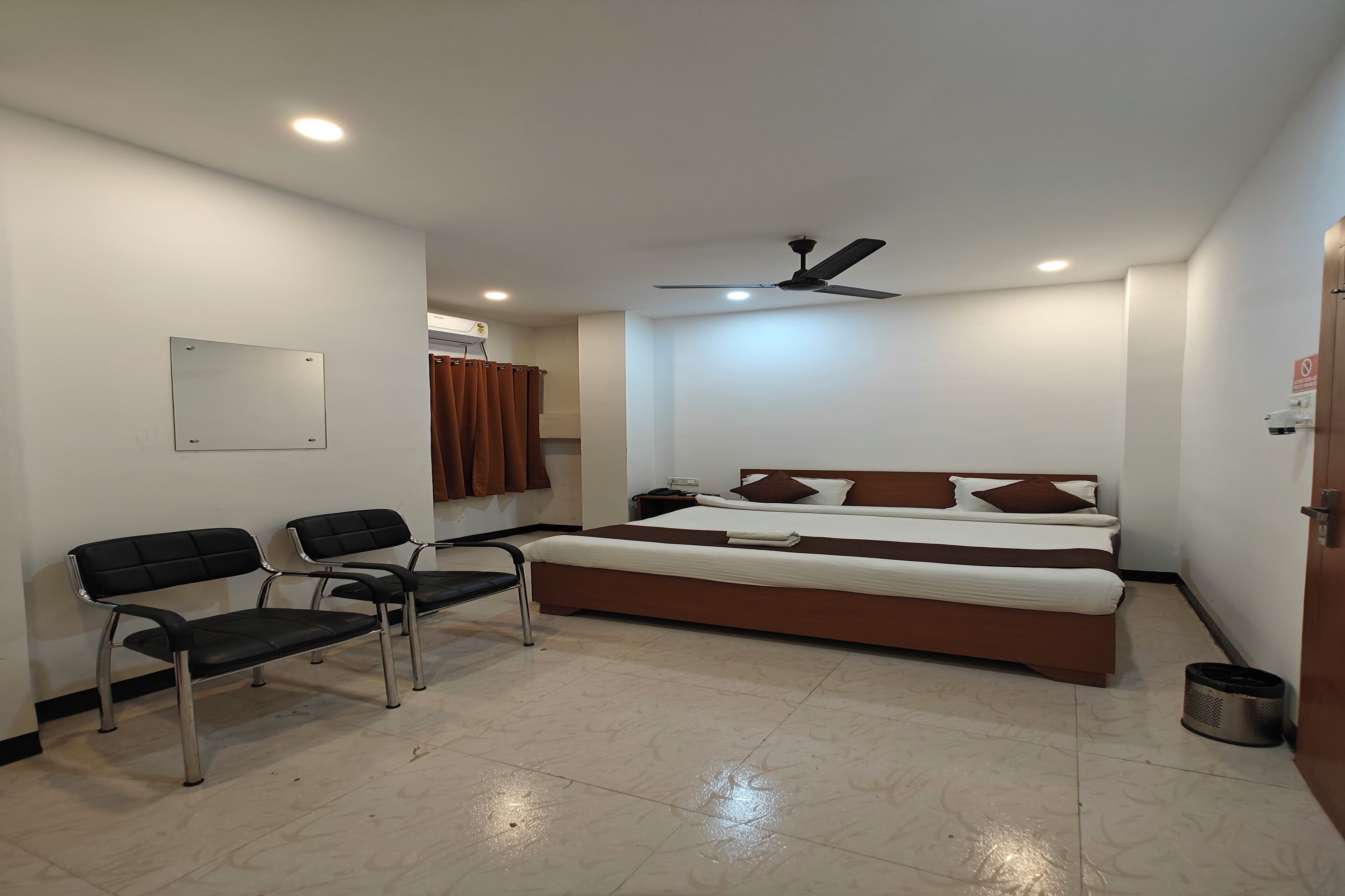 Ein Schlafzimmer mit einem Bett, zwei Stühlen, einem Deckenventilator und einem Mülleimer.