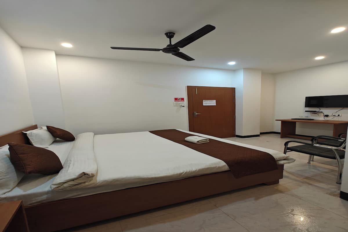 A hotel room with a bed, a ceiling fan, a television, and a desk.