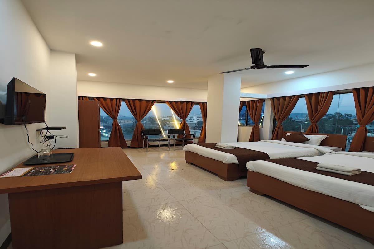 A hotel room with a desk, two beds, a TV, and large windows with curtains.