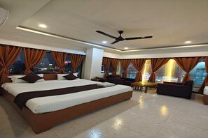 Amplia habitación de hotel con una cama grande, una zona de estar con mesa y vistas a la ciudad de noche.