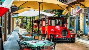 A red vintage train moving through a street with outdoor seating under yellow umbrellas. - 20 Hypolita Street (St. Augustine)