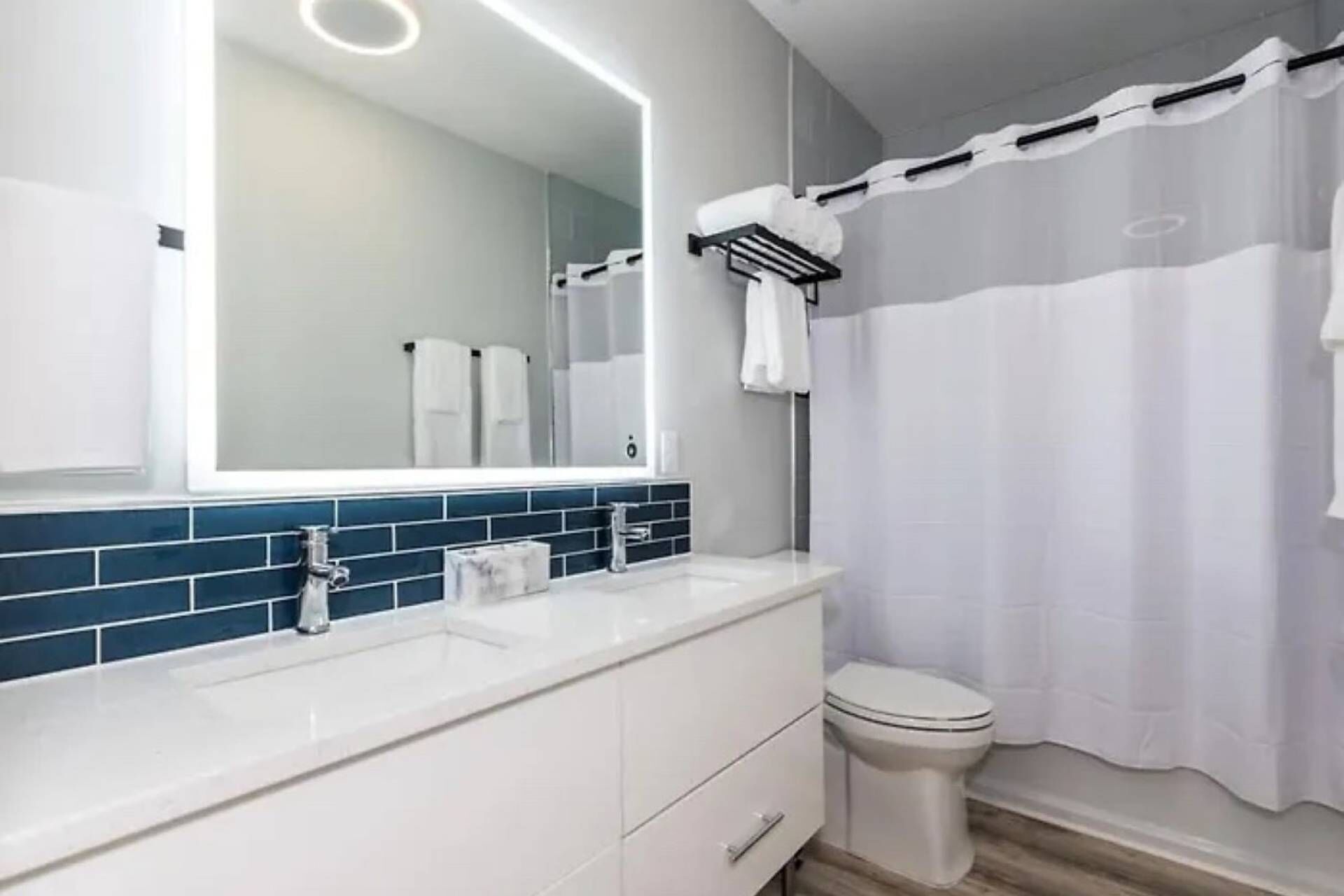 A modern bathroom with a white sink, blue tiles, a large mirror, and a white toilet.
