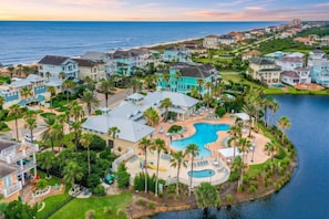 A coastal resort with multiple buildings, a central swimming pool, and a view of the ocean.