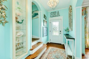 A teal-walled hallway with a wooden staircase, a glass display case with decorative items, and a 'SEA' sign above a door.