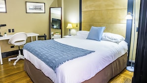 Una habitació d'hotel amb un llit gran, una taula de treball amb una cadira, una làmpada i un mirall.