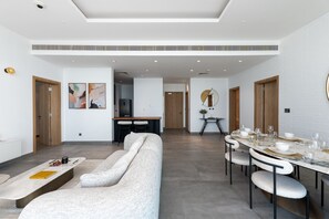Un salon moderne avec un canapé, une table à manger dressée pour six personnes et une cuisine en arrière-plan.