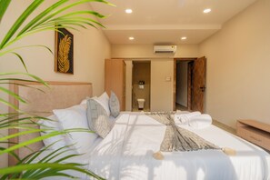 A hotel room with a bed, a bedside table, a nightstand, a wall-mounted air conditioner, and a door leading to a bathroom. - ELIVAAS Kamerios Regalia 2BHK Apartment (Marra)