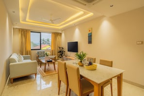 A modern living room with a sofa, dining table, chairs, a TV, and a large window with curtains.