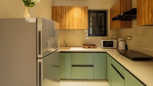 A modern kitchen with a stainless steel refrigerator, a microwave, and wooden cabinets. - ELIVAAS Kamerios Regalia 2BHK Apartment (Marra)
