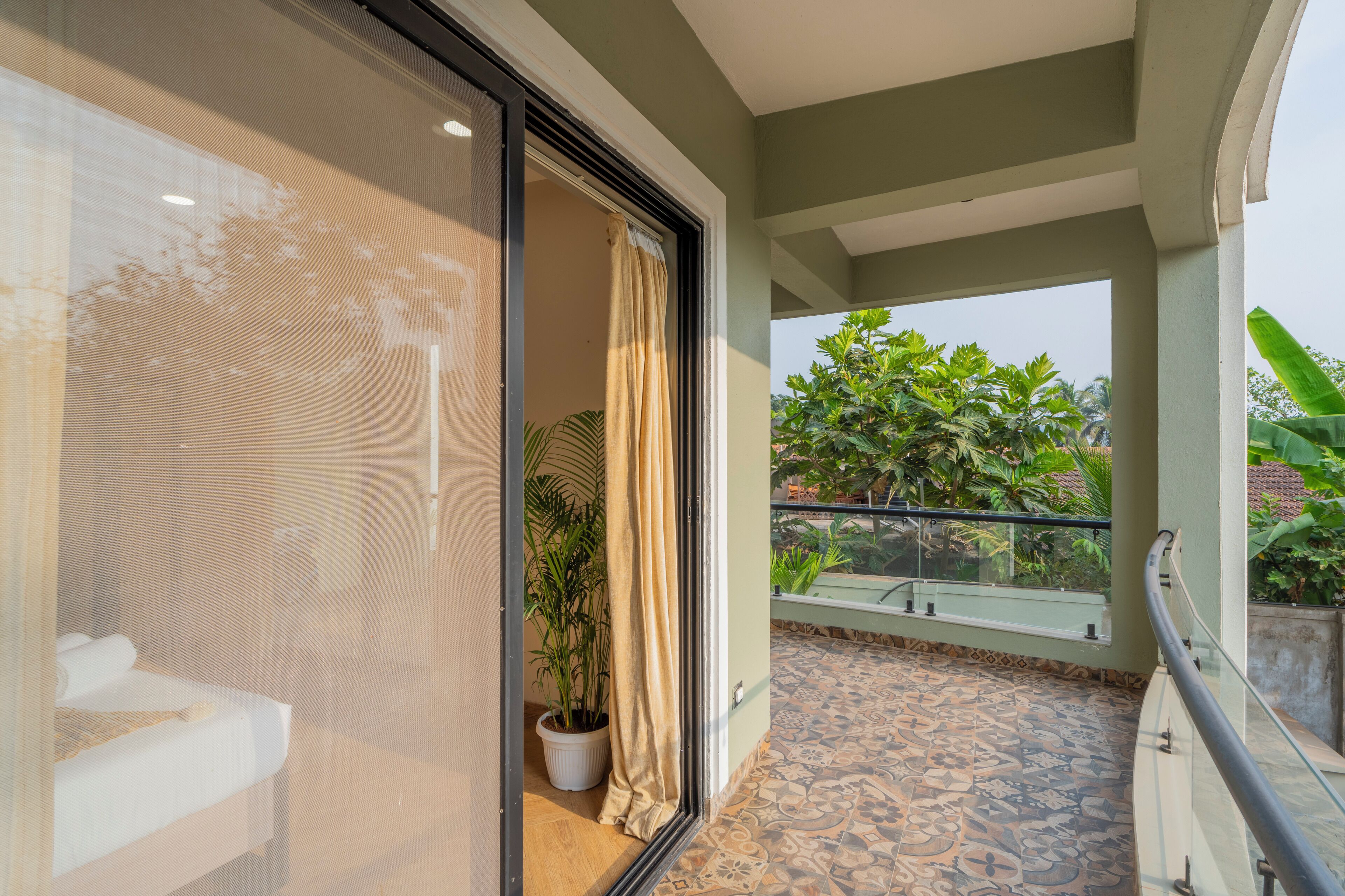 A balcony with patterned flooring, a potted plant, and a view of greenery.