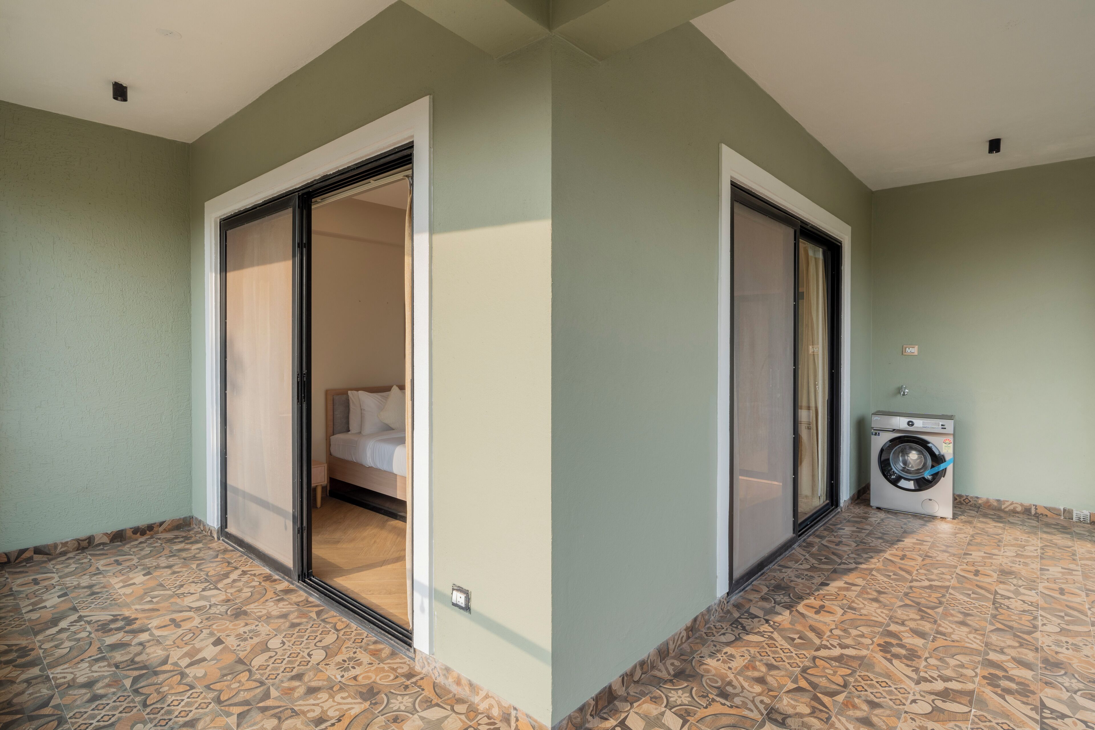 A room with a bed, a sliding door, a washing machine, and patterned floor tiles.