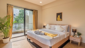 A modern hotel room with a large bed, a nightstand, a potted plant, and a view through a sliding glass door. - ELIVAAS Kamerios Regalia 2BHK Apartment (Marra)