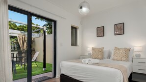 A bedroom with a bed, a nightstand, a lamp, and a sliding glass door leading to an outdoor area with a table and chairs. - Modern 3-Bed Home , Canal Views & Parking (Cape Town)