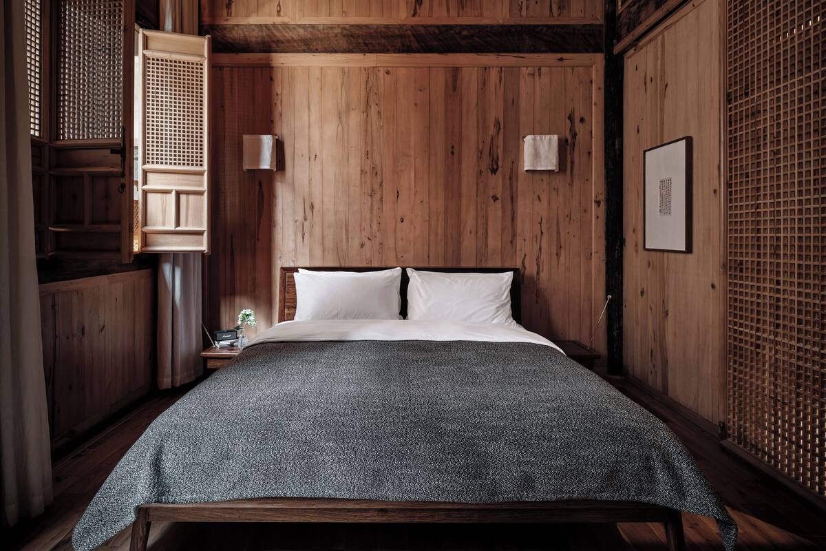 A wooden room with a bed, a nightstand, and a wall-mounted shelf.