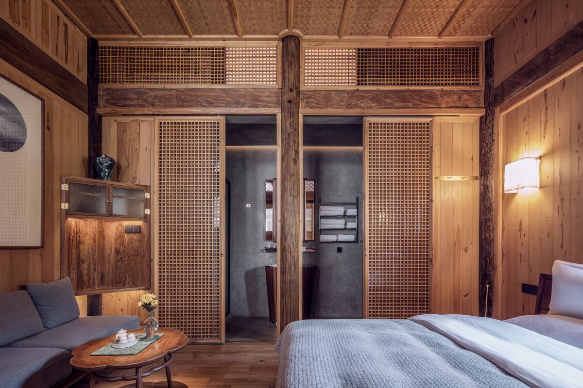 A traditional Japanese-style room with tatami flooring, a low wooden bed, a sofa, a small table with a vase, and sliding doors with a lattice design.