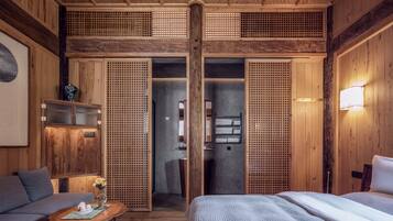 Een traditionele Japanse kamer met tatami vloerbedekking, een laag houten bed, een bank, een kleine tafel met een vaas en schuifdeuren met een lattenpatroon.